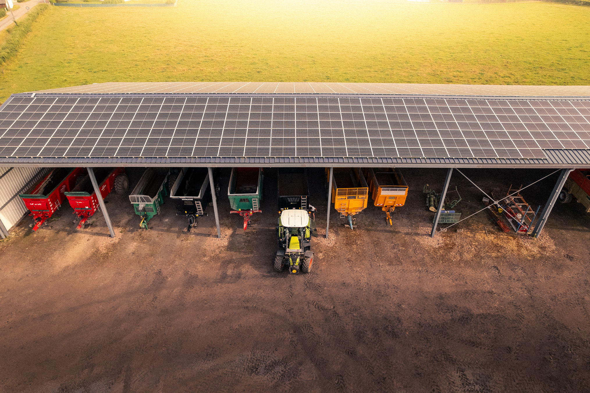 Hangar agricole avec panneaux solaires et matériel de ferme en stockage.