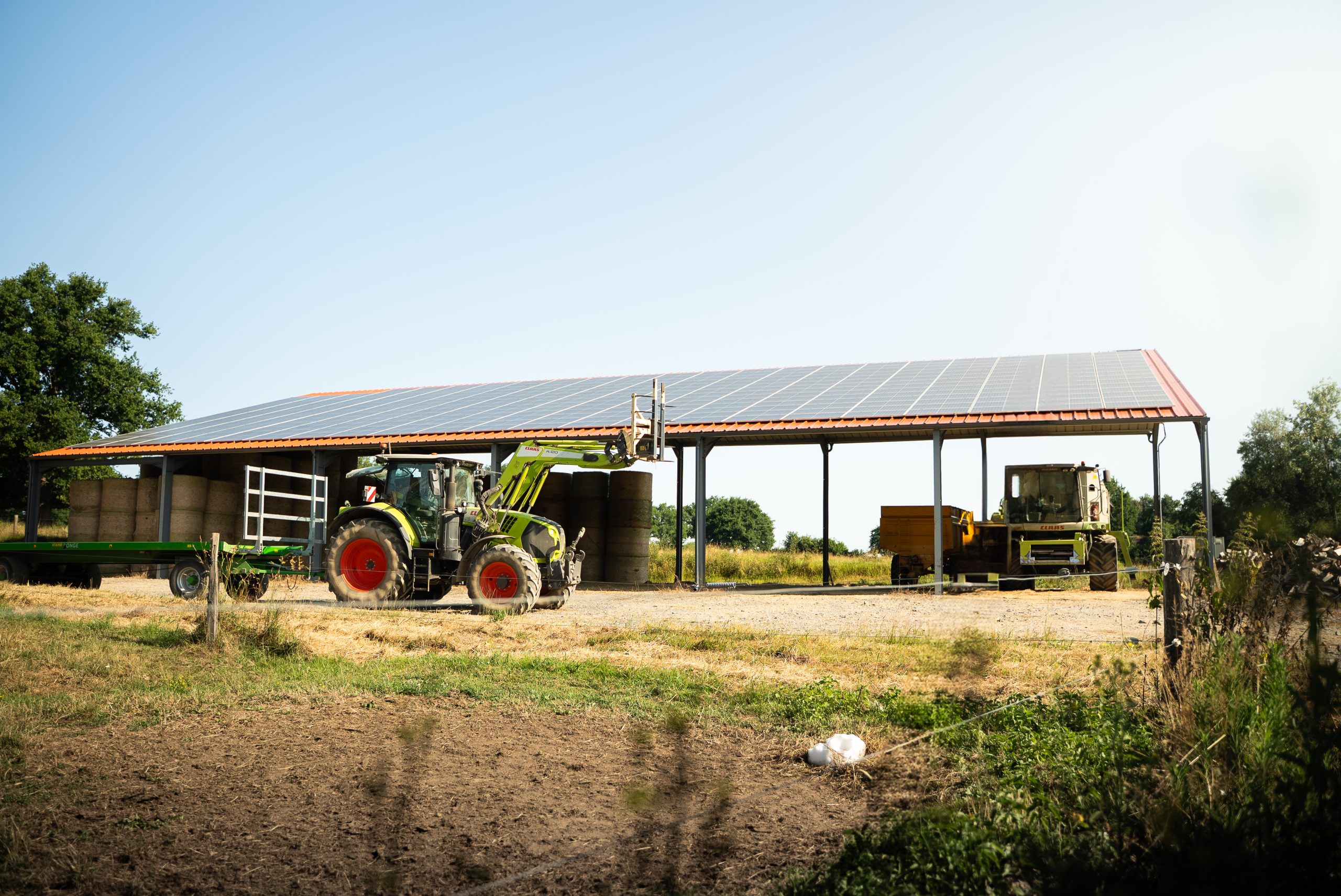 Hangar agricole avec panneaux solaires, tracteur vert et bottes de foin sur une ferme.